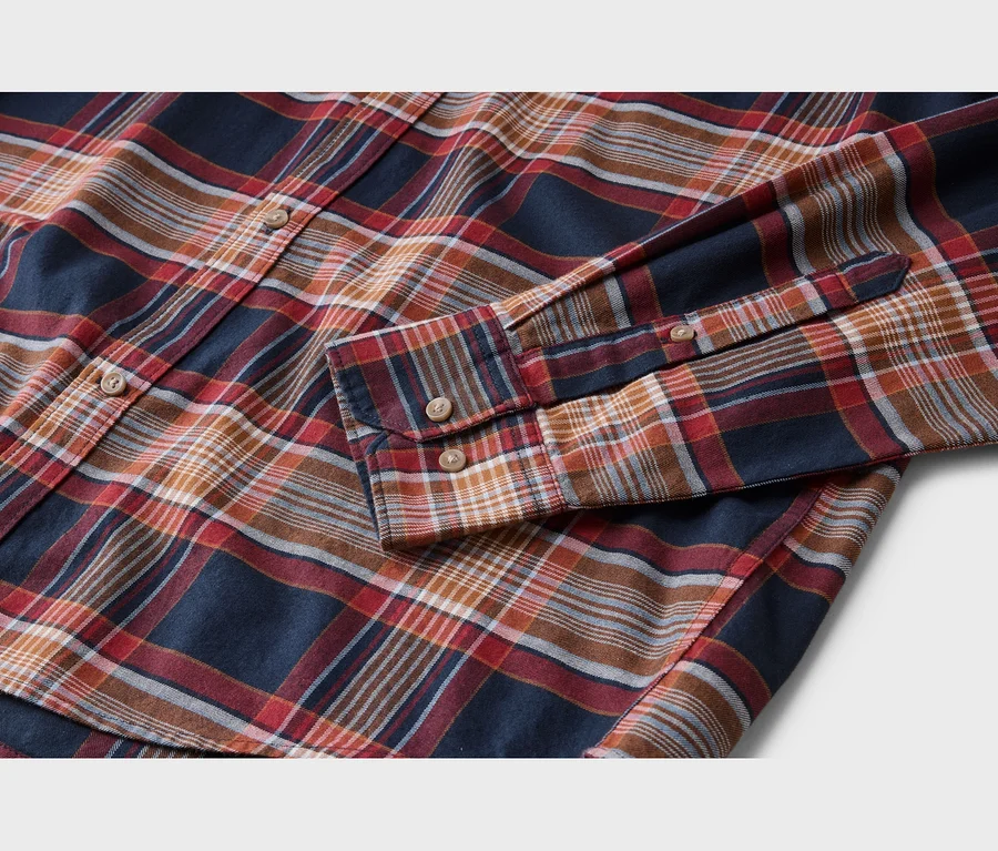 Chemise à carreaux bleu marine, rouge, orange et blanc avec des boutons marron clair, posée à plat.