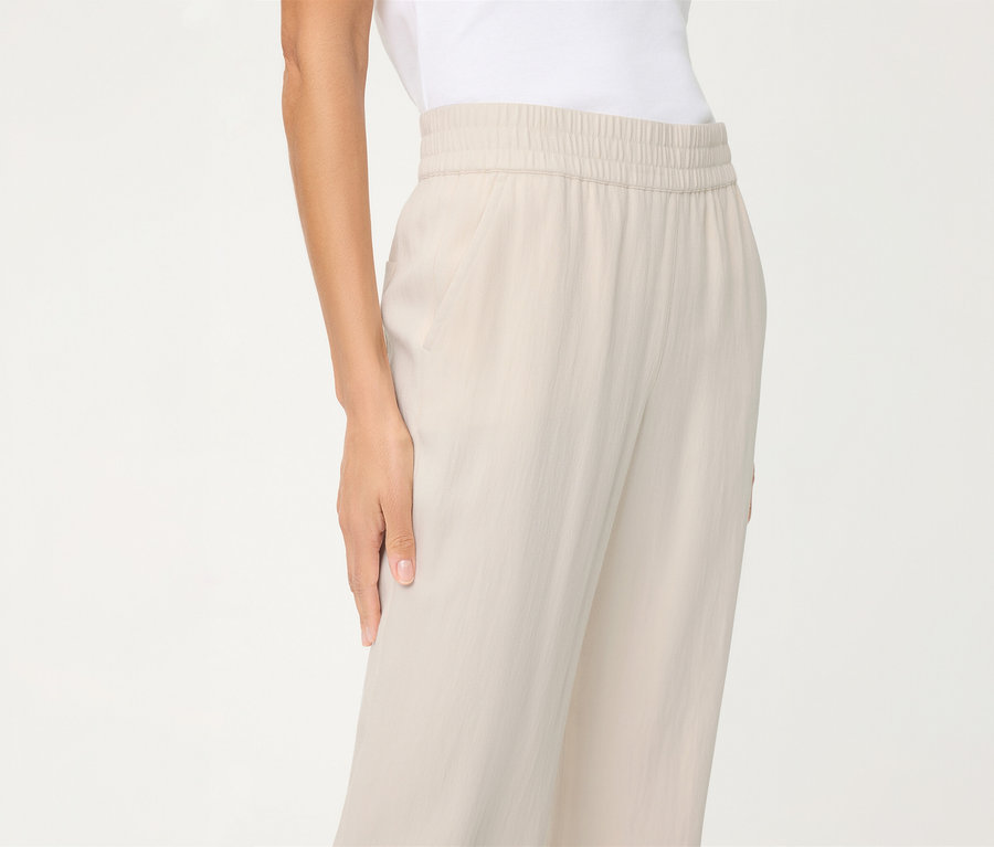 Personne portant un pantalon en lin Olsen beige clair à taille élastique et un haut blanc. Une main est visible.