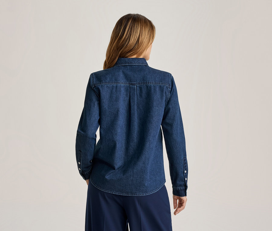 Femme de dos, aux longs cheveux châtains clairs, portant une chemise en jean bleu foncé à manches longues et un pantalon large bleu foncé.