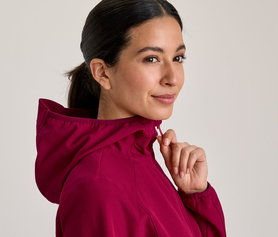 Femme en veste à capuche magenta, la fermant et regardant par-dessus son épaule.