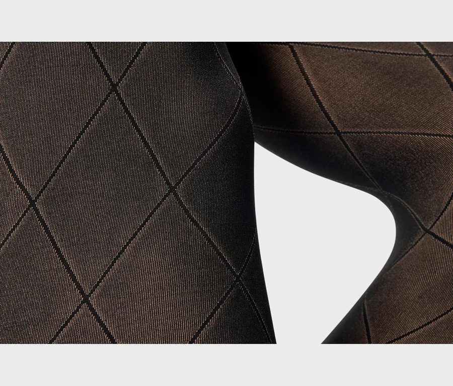 Gros plan d'un tissu marron avec un motif losanges noir, courbé autour d'une forme, sur fond blanc.