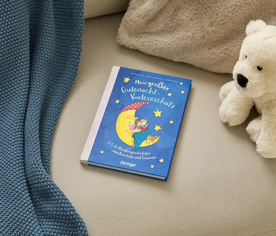 Un livre pour enfants bleu intitulé « Mein großer Gutenacht-Vorleseschatz » avec une illustration de lune, une couverture bleue et un ours en peluche blanc sur un canapé beige.