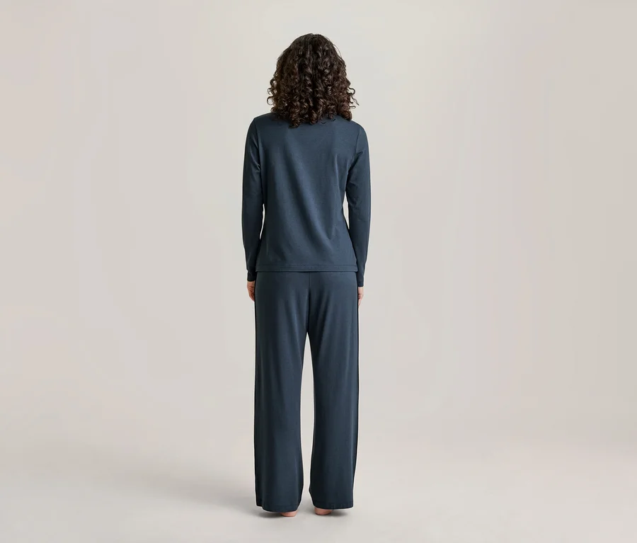 Une personne aux cheveux bouclés foncés se tient dos à la caméra, vêtue d'un haut à manches longues bleu foncé et d'un pantalon large assorti.