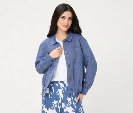 Une femme porte une veste en jean Olsen bleue par-dessus un haut blanc et une jupe à motifs bleu et blanc.