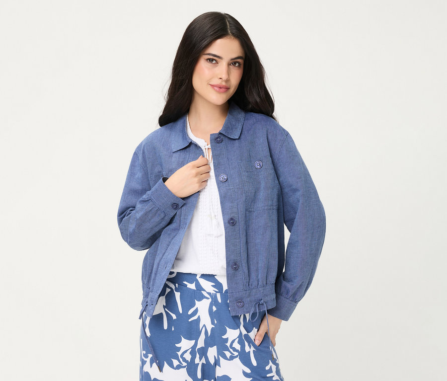Une femme porte une veste en jean Olsen bleue par-dessus un haut blanc et une jupe à motifs bleu et blanc.