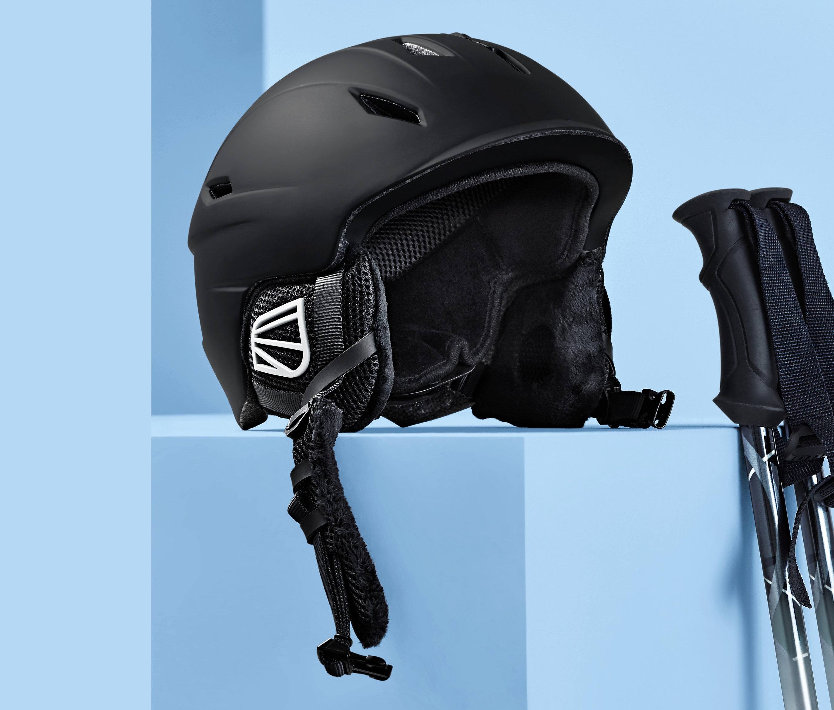Casque de ski et snowboard In-Mould noir et bâtons de ski sur fond bleu.