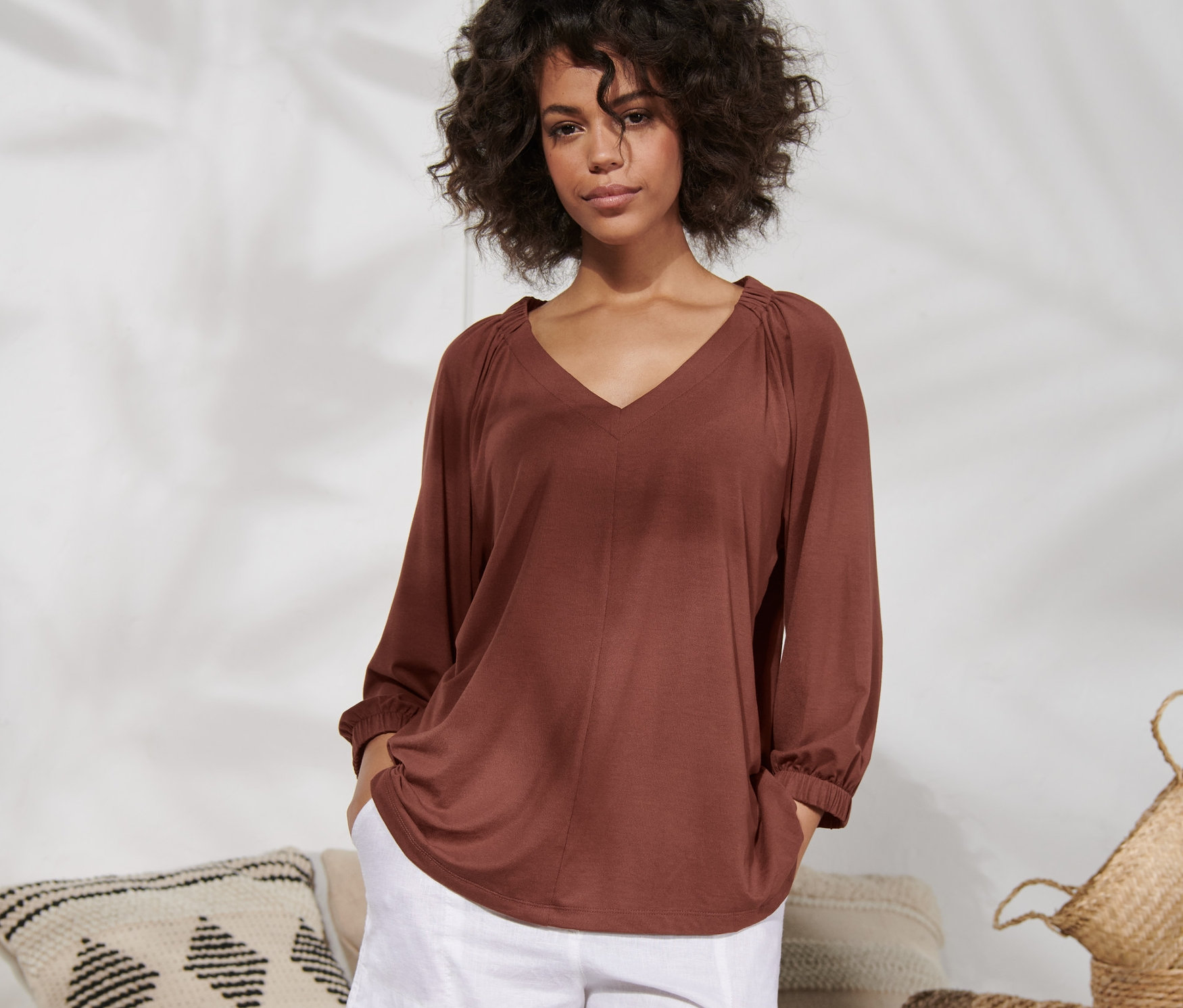 Femme posant dans une chemise froncée couleur terre cuite et un short blanc.