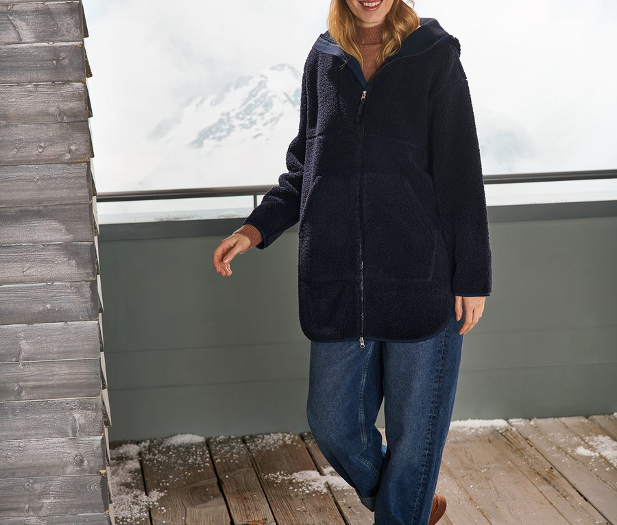 Une femme portant un manteau oversize en peluche, un jean et un bonnet.