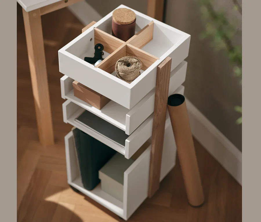 Un caisson à roulettes blanc avec quatre tiroirs est placé à côté d'un bureau. Des fournitures de bureau se trouvent dans le tiroir supérieur.