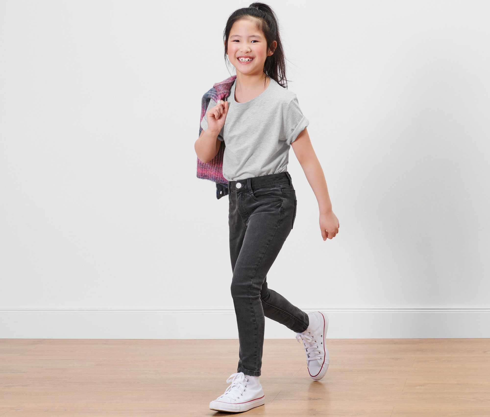 Une fillette souriante pose en jean taille haute gris – Fit « Lotta » et un t-shirt gris.