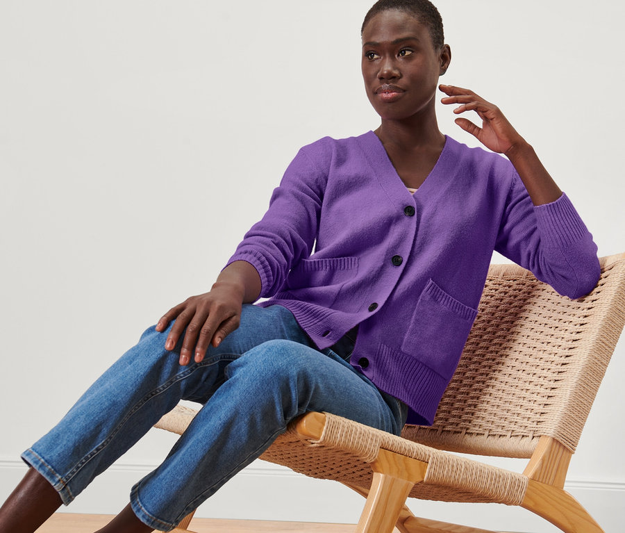 Une femme est assise sur une chaise et porte une jaquette en maille violette avec de la laine.