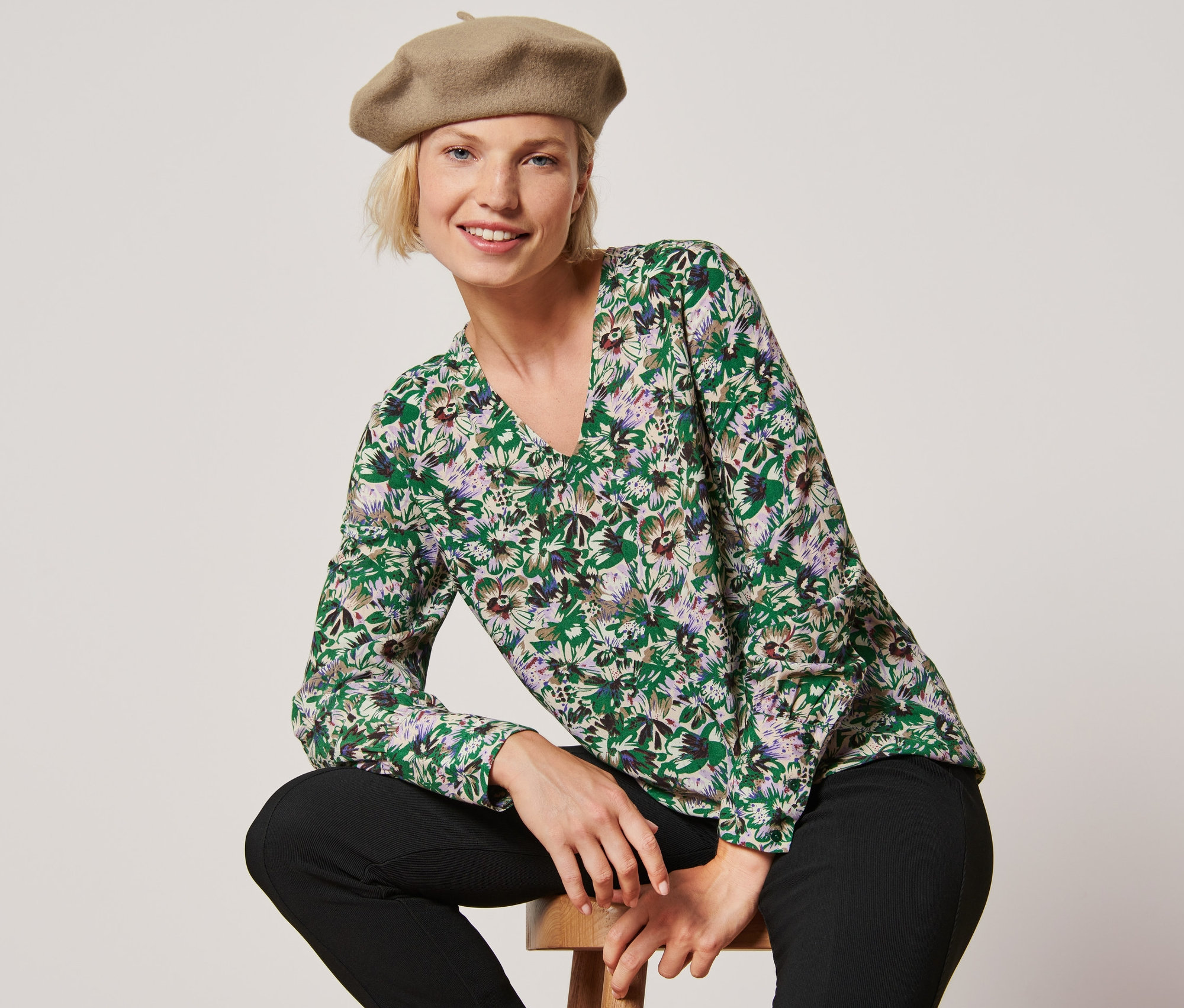 Une femme est assise sur un tabouret et porte une blouse à imprimé intégral et un béret.