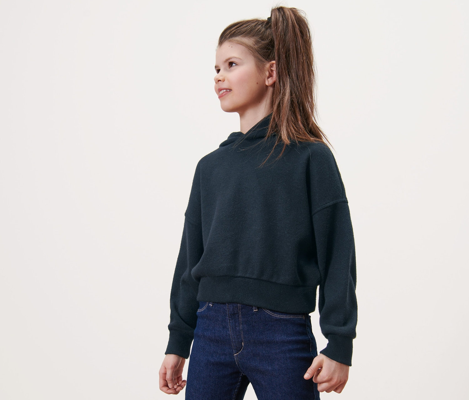 Une fille porte un sweat à capuche en maille pour enfant et un jean.