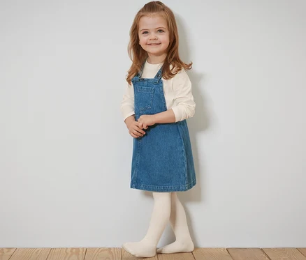 Fillette souriante posant en robe-salopette pour enfant.