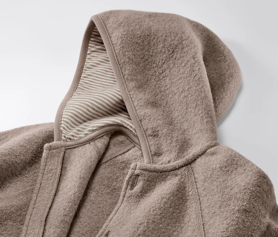 Gros plan sur une combinaison marron pour bébé en laine mérinos avec capuche et doublure rayée.