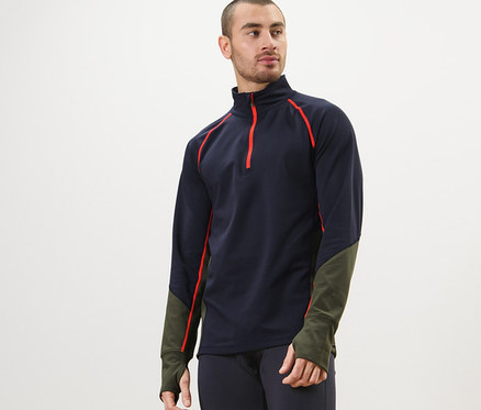 Un homme portant un t-shirt technique thermique à manches longues, un legging bleu marine, pose.