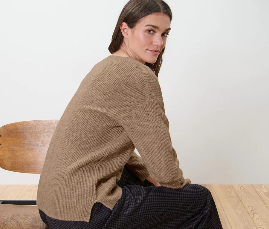 Femme assise sur une chaise en bois portant un pull camel en grosse maille.