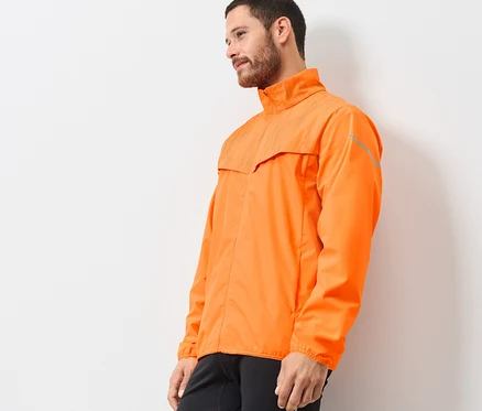 Un homme portant une veste de course coupe-vent orange néon, debout de profil.