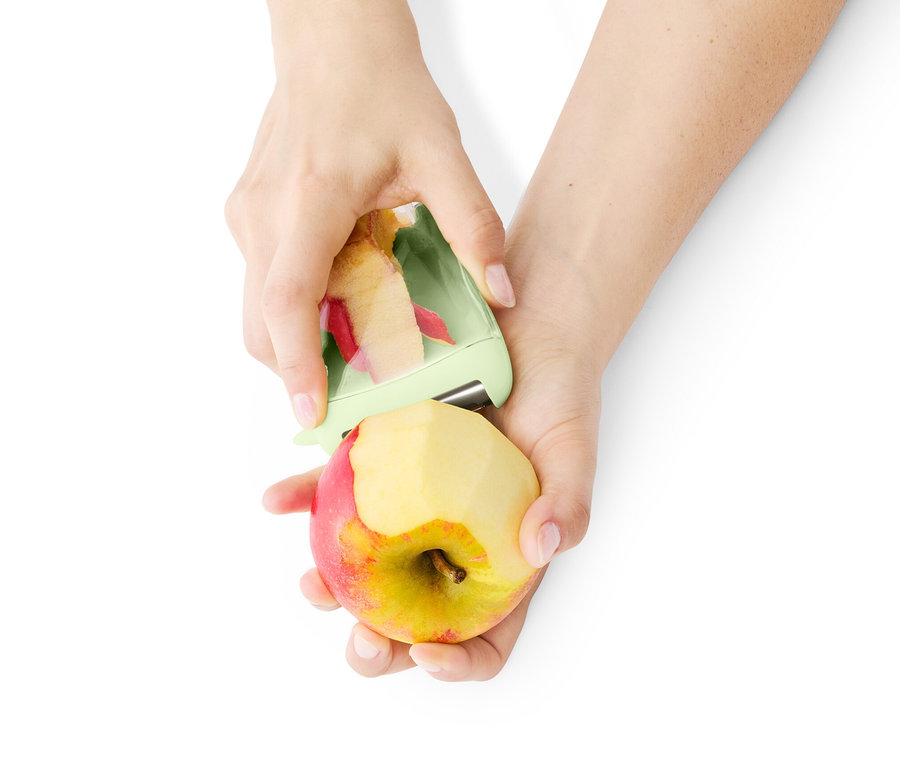 Une personne pèle une pomme avec un éplucheur universel avec récipient collecteur.