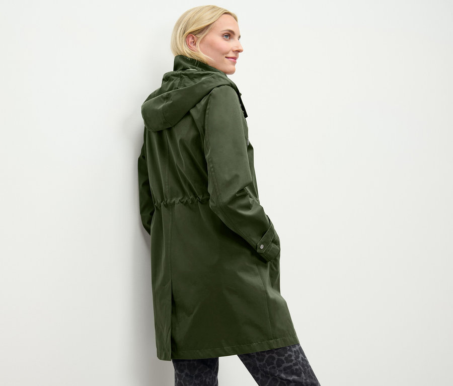 Une femme pose dans une parka à capuche verte.