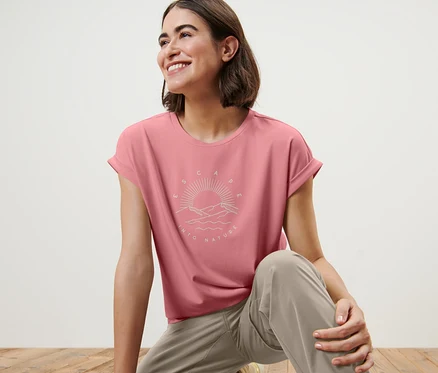 Une femme sur un plancher en bois porte un t-shirt à imprimé rose.