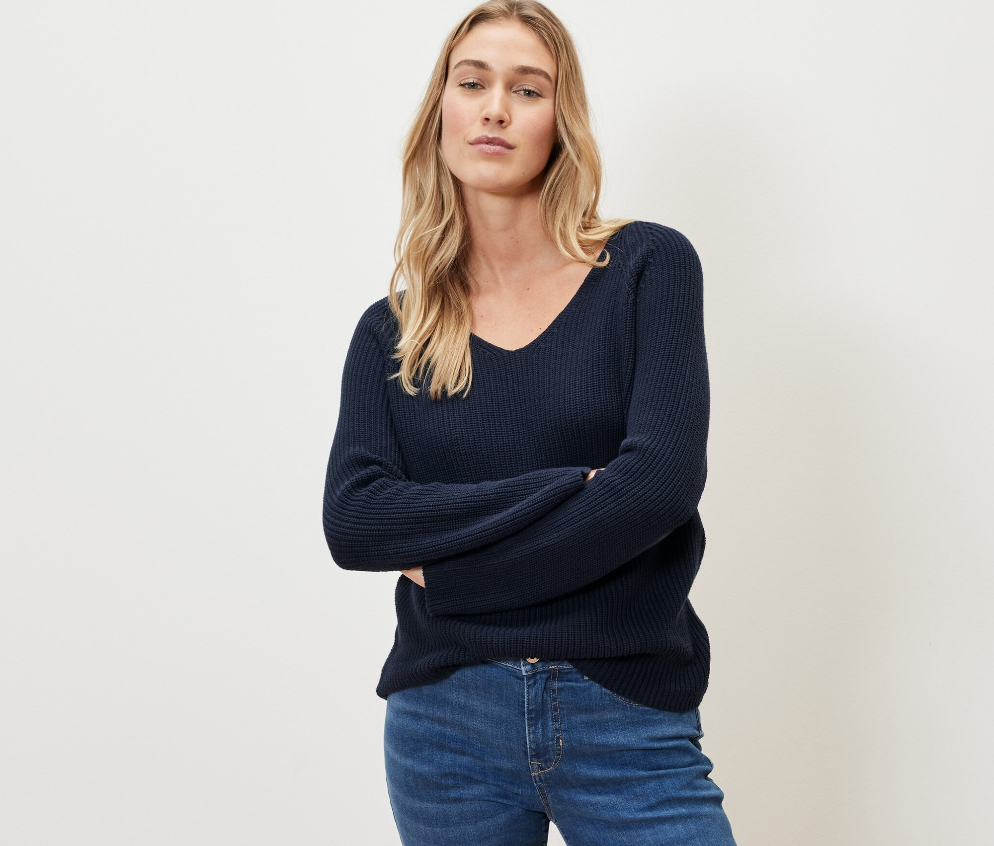 Une femme pose, portant un pull en maille bleu foncé.