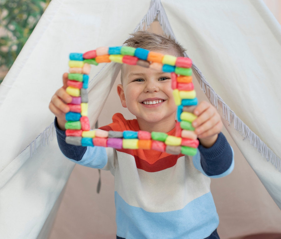 Un garçon est assis dans un tipi et tient un carré coloré de l'ensemble PlayMaisR dans ses mains.