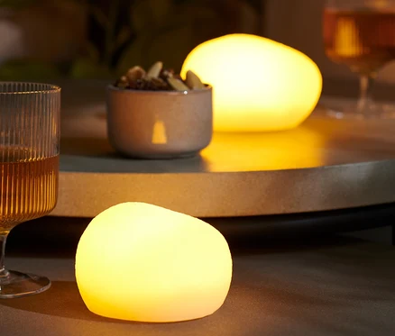Sur une table, il y a deux pierres décoratives à LED, un verre avec une boisson et un bol de noix.