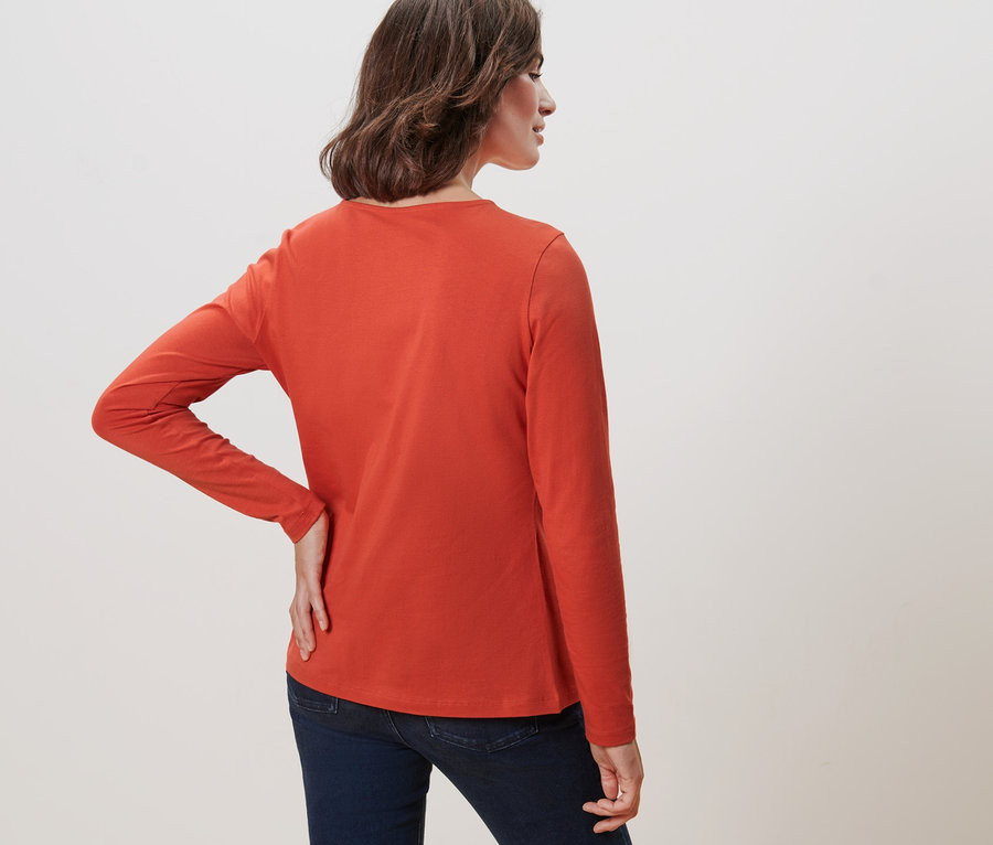 Une femme, vue de dos, porte un t-shirt orange à manches longues.