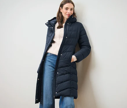 Femme posant dans un manteau matelassé à capuche bleu foncé.