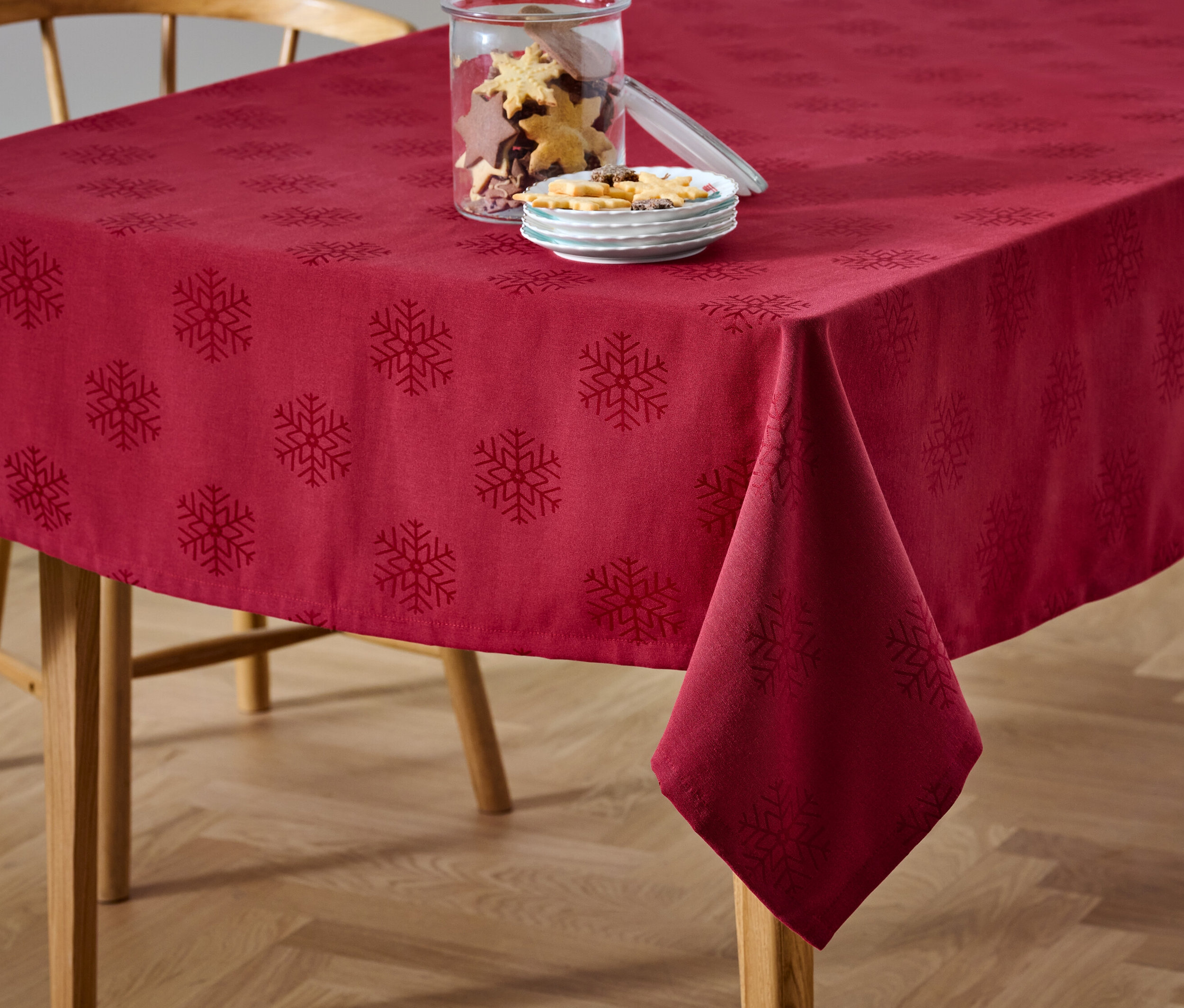 Une nappe jacquard rouge avec un motif de flocons de neige est posée sur une table à côté d'un bocal de biscuits et d'une assiette de bonbons.