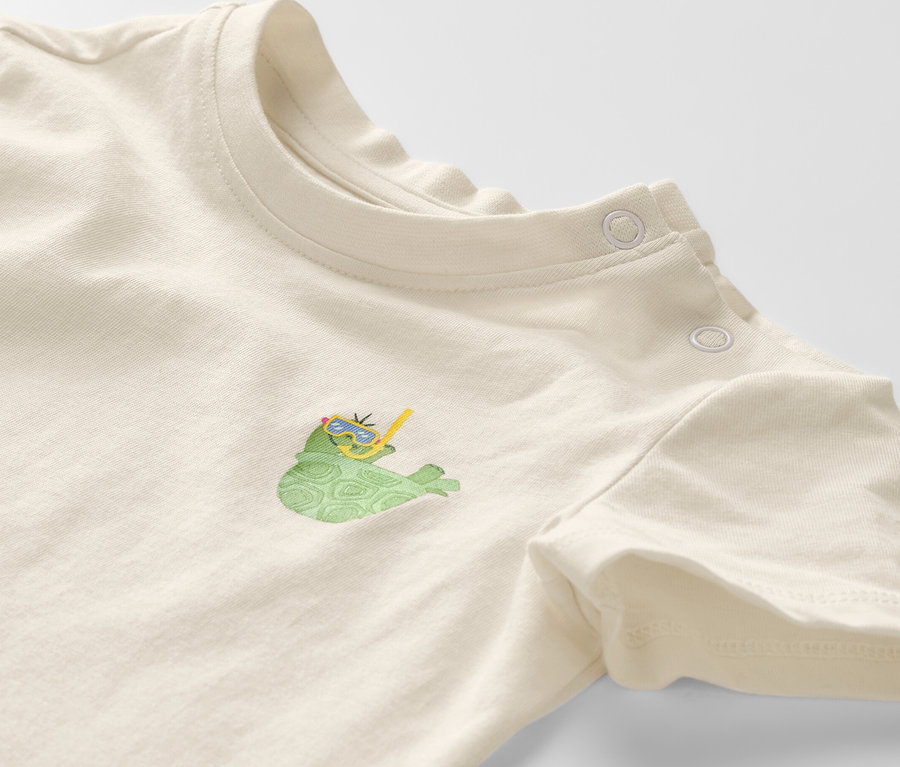 Gros plan sur un t-shirt à manches courtes pour enfant, orné d'un motif de tortue portant des lunettes et un tuba.