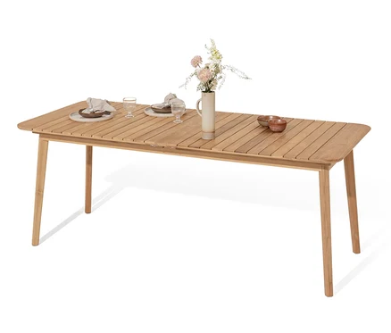 Une table en teck à double rallonge est dressée avec des assiettes, des verres et des serviettes. Un vase avec des fleurs est placé au centre de la table.