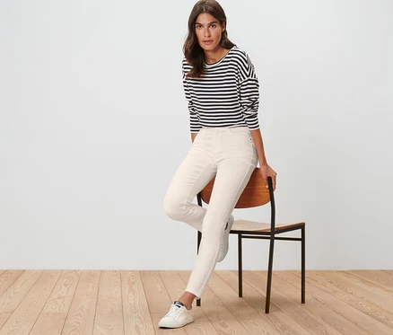 Femme assise sur une chaise portant un jean coloré coupe « Emma » blanc crème et un t-shirt rayé.
