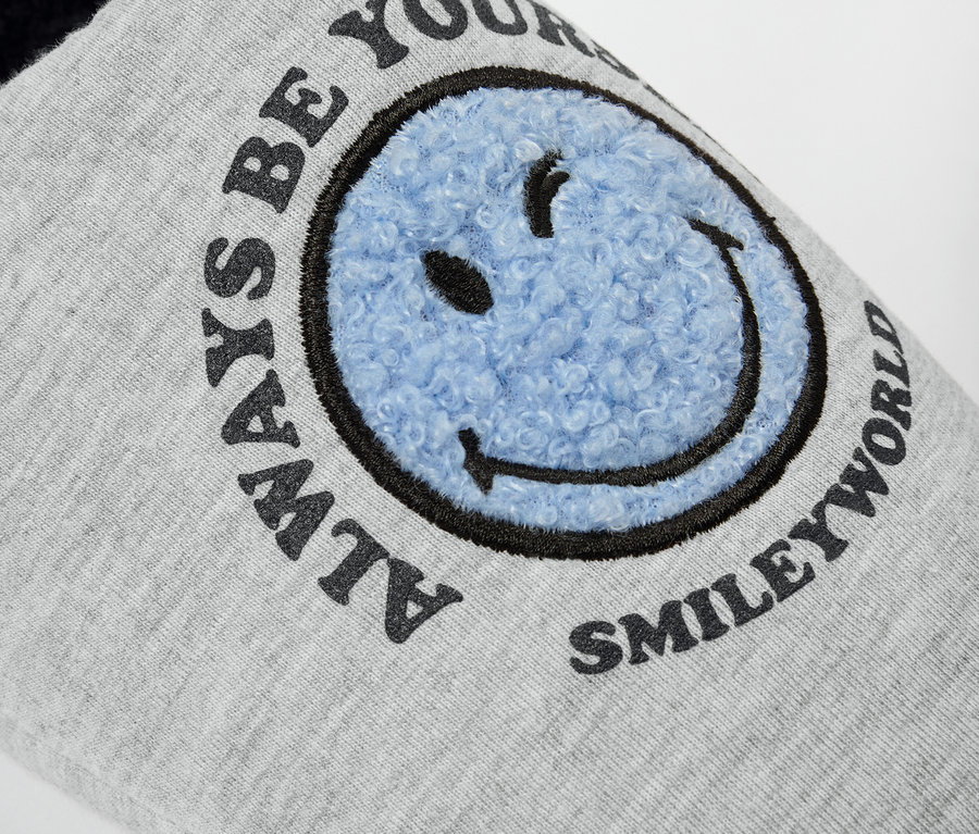 Gros plan sur une pantoufle grise SMILEYWORLD® avec un smiley bleu.