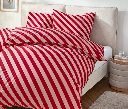 Lit avec des draps rayés rouge et blanc, table de chevet avec boisson et tapis.