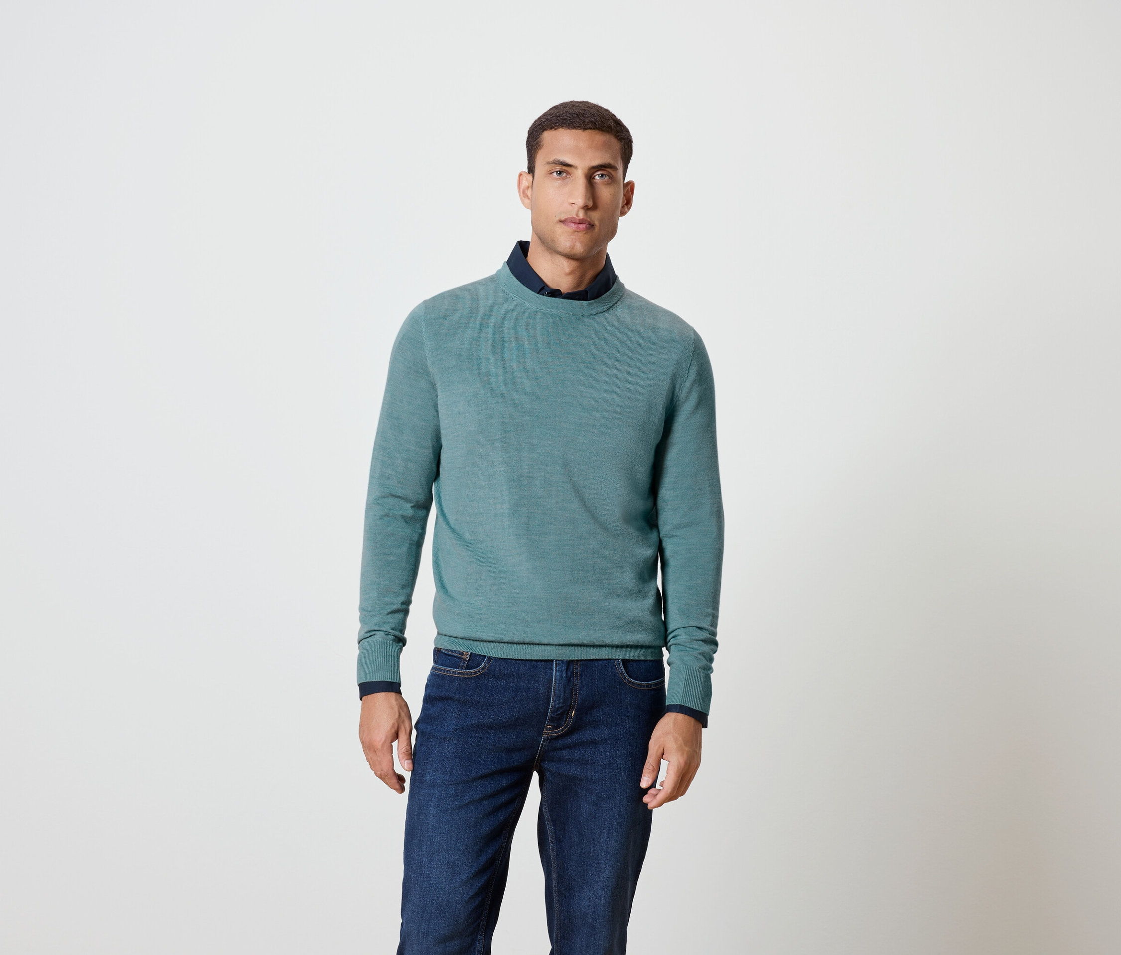 Un homme pose en pull bleu et jeans.