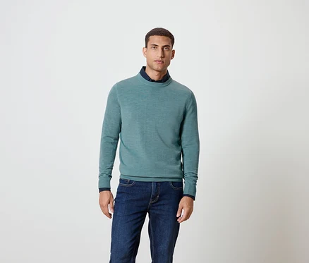 Un homme pose en pull bleu et jeans.