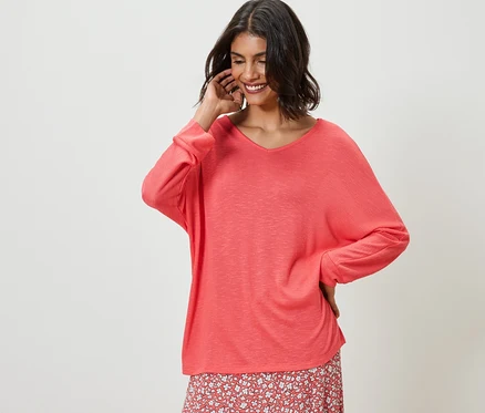 Femme posant dans un t-shirt corail à manches chauve-souris et une jupe à fleurs.