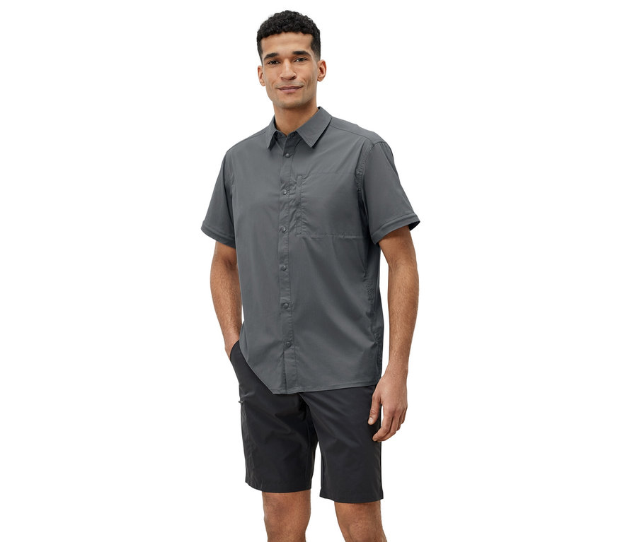Un homme pose en chemise d’extérieur grise et short noir.