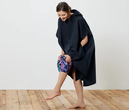 Une femme souriante enfile un poncho de change bleu marine.