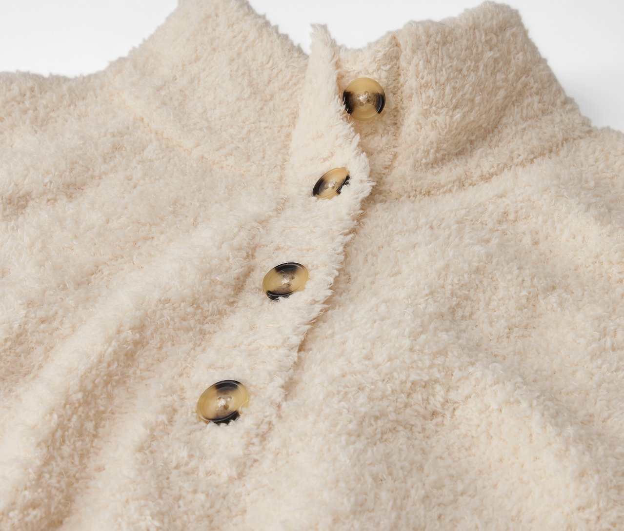 Gros plan d'une veste duveteuse crème avec des boutons.