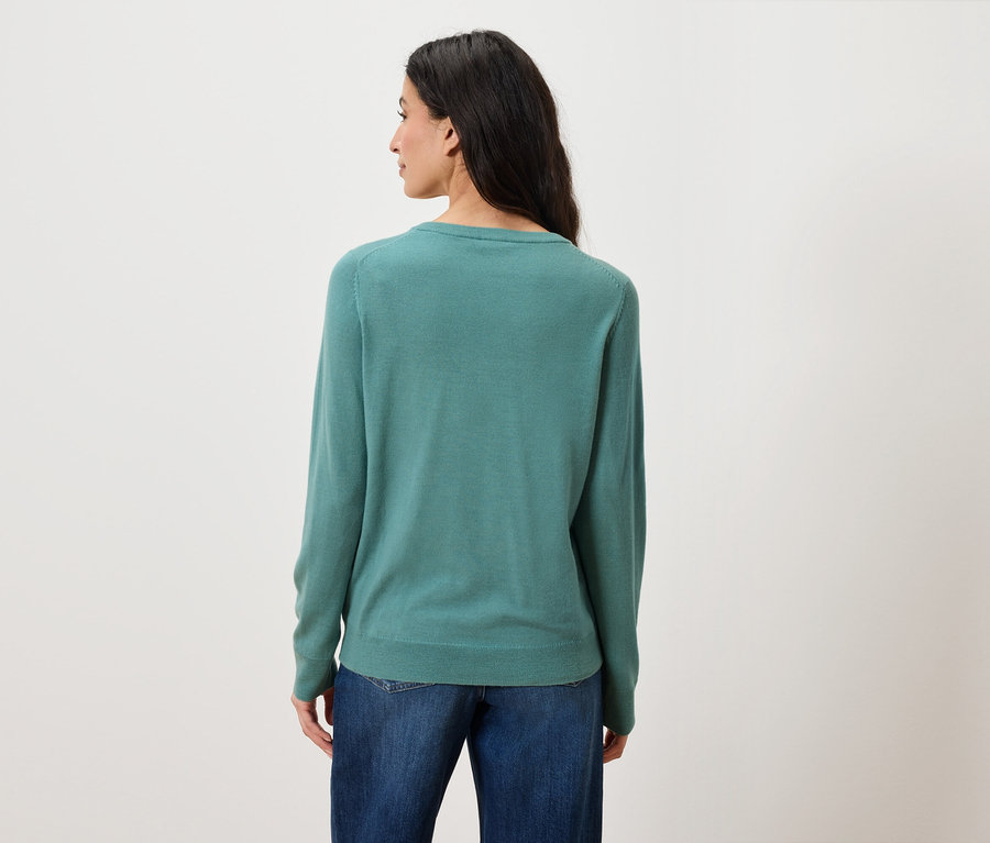 Vue de dos d'une femme aux longs cheveux foncés portant un jean bleu et un pull vert.