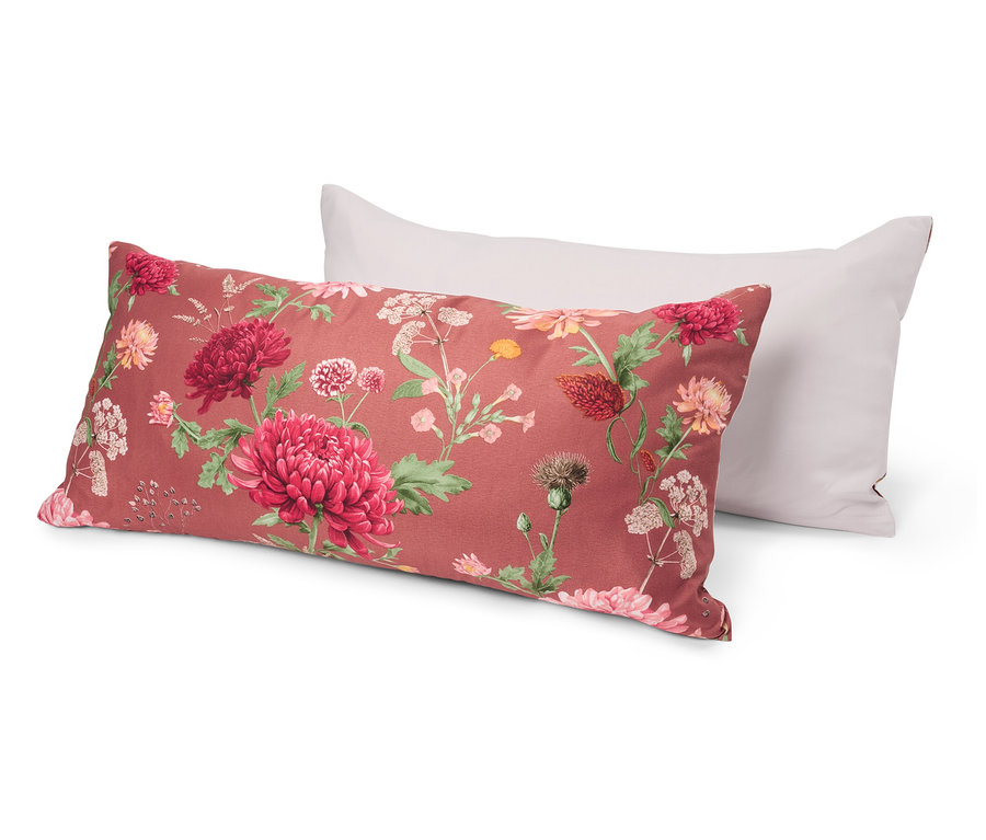 Deux oreillers sont posés l’un sur l’autre. L’oreiller inférieur a un motif floral avec des fleurs rouges et roses sur un fond rouge. L’oreiller supérieur est blanc.