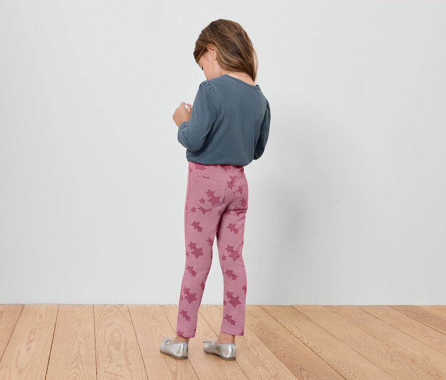 Fillette portant un legging rose à motifs floraux et un t-shirt bleu à manches longues, dos à la caméra.
