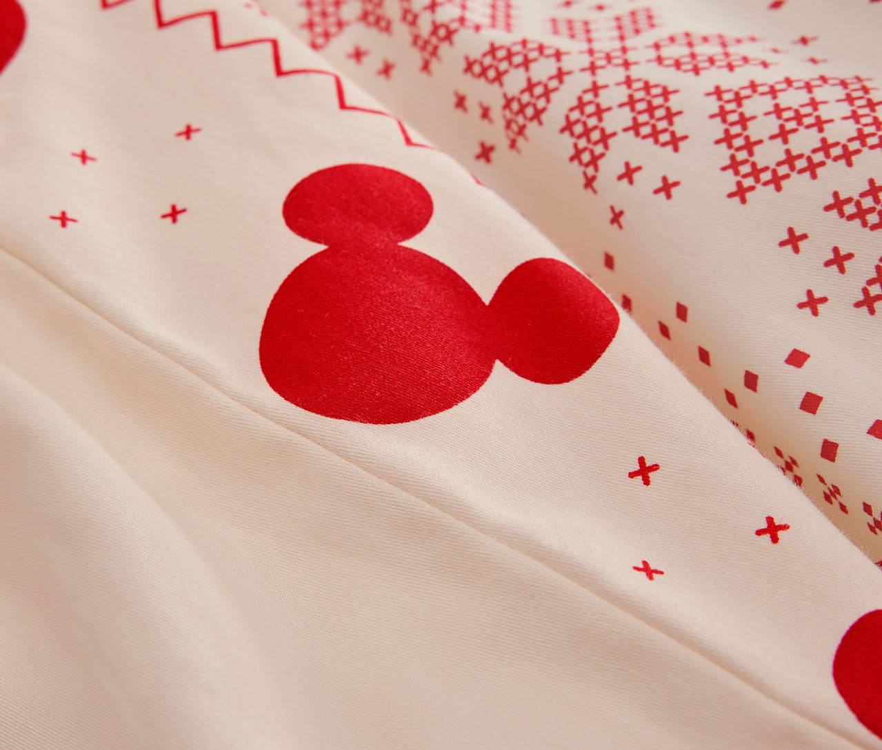Détail de linge de lit blanc avec motif Mickey Mouse rouge et motifs de Noël.