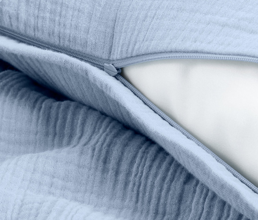 Gros plan d'une taie d'oreiller bleu clair avec une fermeture éclair, révélant le rembourrage blanc de l'oreiller.