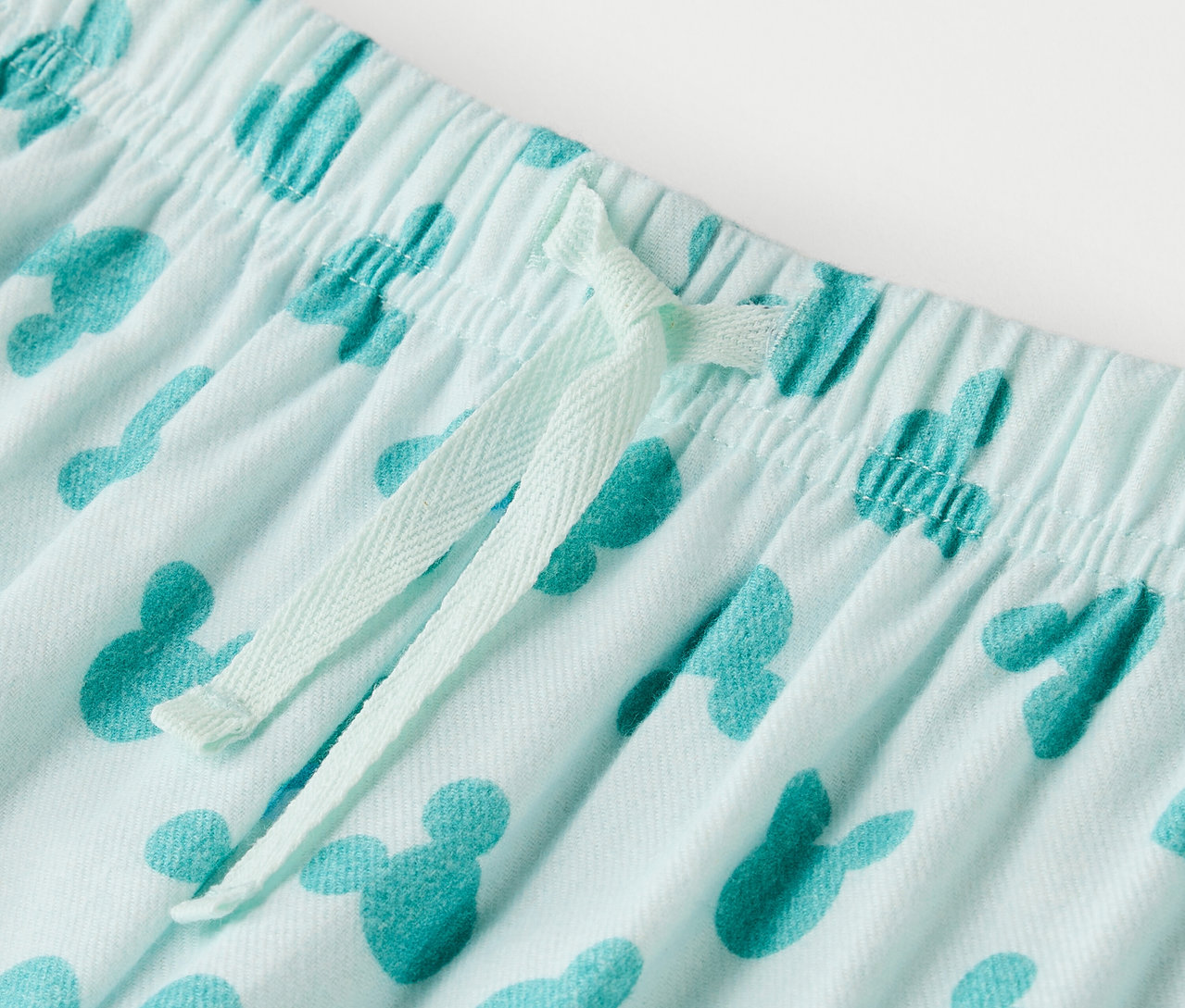 Détail d'un pantalon bleu clair avec imprimé Mickey Mouse et cordon de serrage.