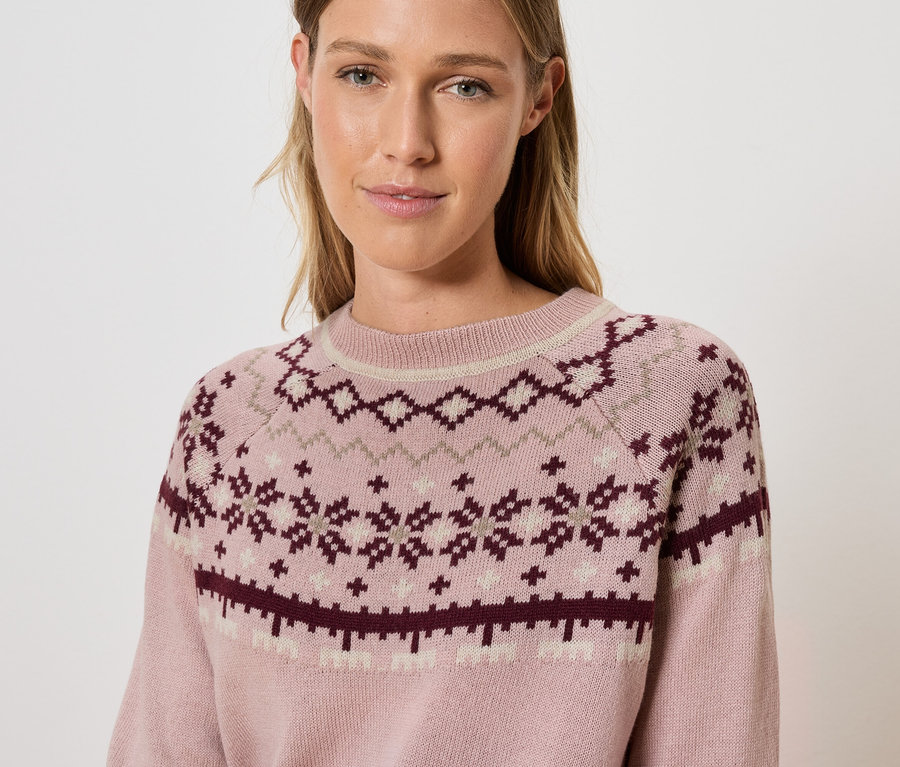 Une femme porte un pull rose à motifs.
