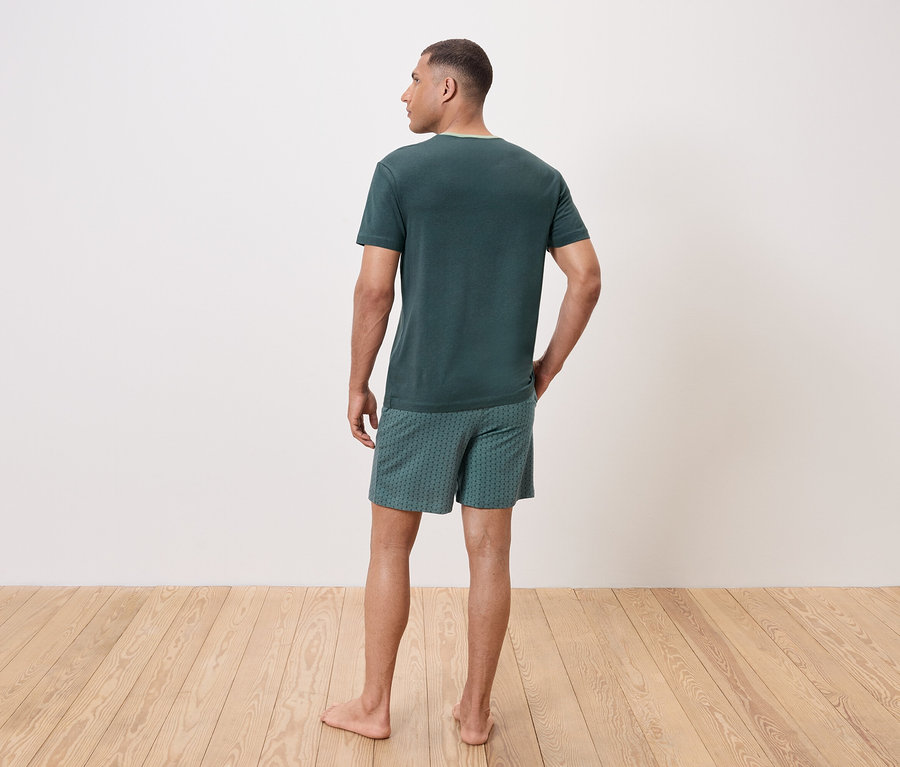 Un homme vu de dos porte un t-shirt vert et un short à motifs.